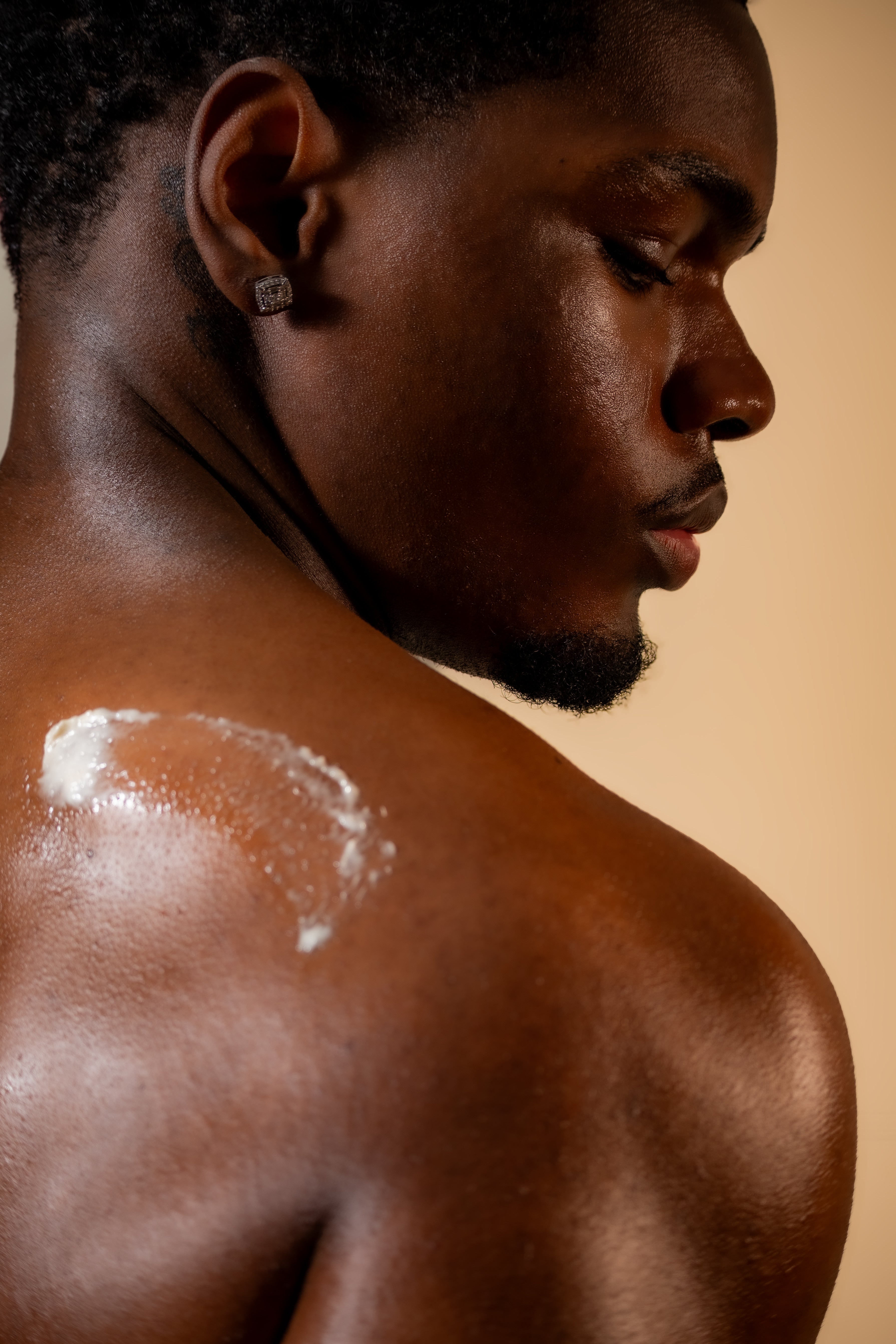 Man with Abiara Skin Body Butter on his shoulder against a beige background