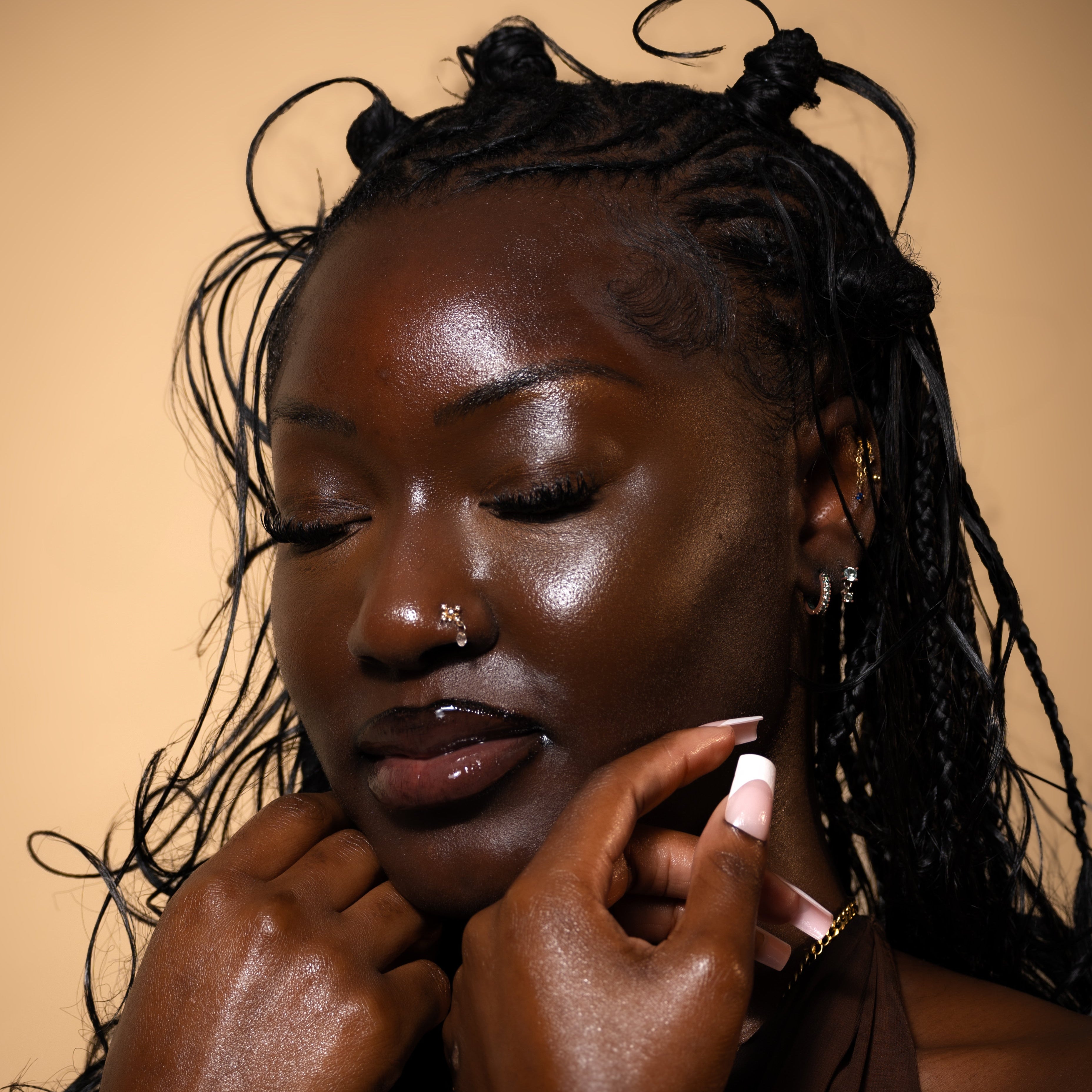 Woman with glowy skin by Abiara Skin products touching her face against a beige background